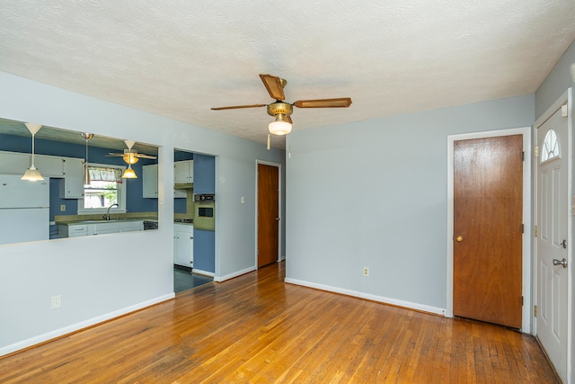 unfurnished living room with a textured ceiling, ceiling fan, sink, and hardwood / wood-style flooring