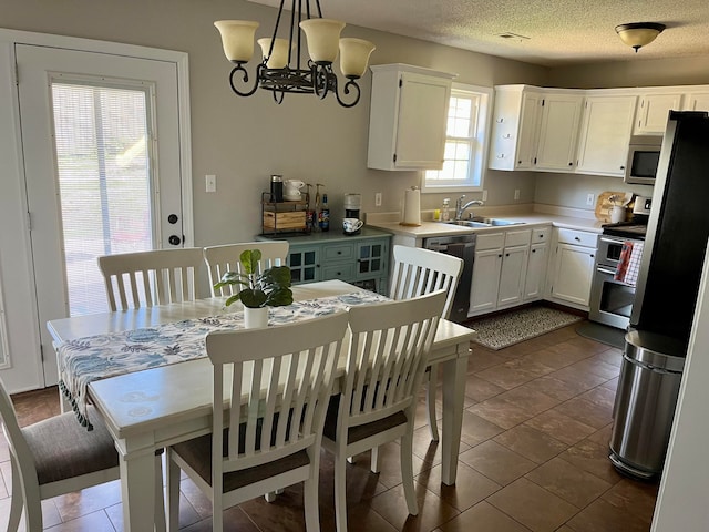 kitchen featuring sink, a textured ceiling, white cabinetry, stainless steel appliances, and decorative light fixtures