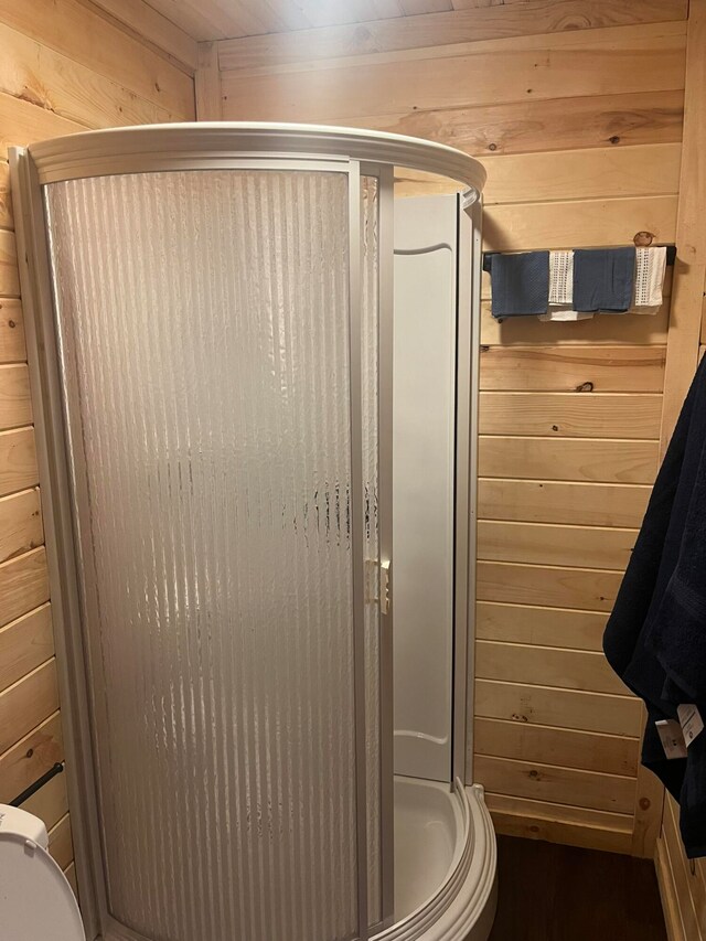 bathroom featuring a shower with shower door, toilet, and wood walls