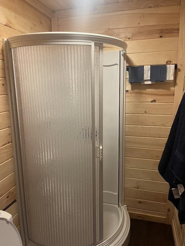 bathroom with wood walls, a stall shower, and toilet