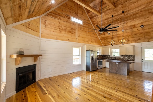 kitchen with high vaulted ceiling, white cabinets, hanging light fixtures, light hardwood / wood-style floors, and stainless steel appliances