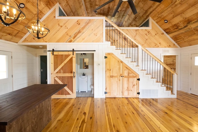 interior space with hardwood / wood-style floors, wooden ceiling, ceiling fan with notable chandelier, wooden walls, and a barn door