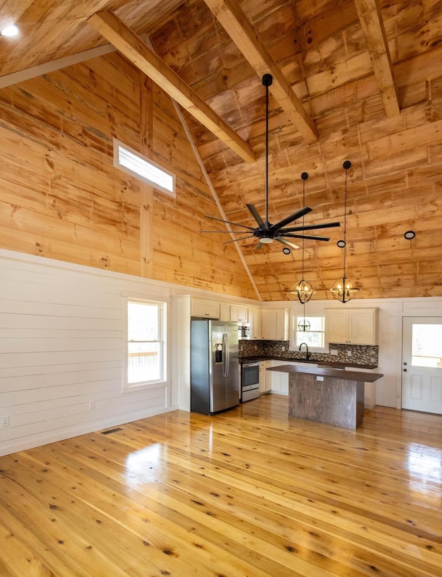 kitchen with stainless steel appliances, wooden walls, pendant lighting, high vaulted ceiling, and light hardwood / wood-style floors