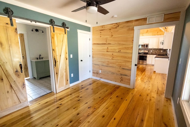 bedroom with wood walls, a barn door, sink, and light hardwood / wood-style flooring