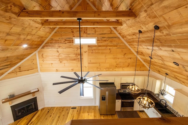 interior space featuring beam ceiling, wood walls, pendant lighting, appliances with stainless steel finishes, and light wood-type flooring