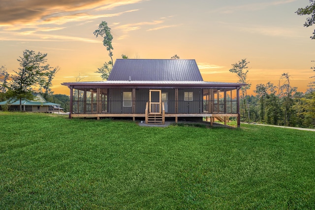 back house at dusk with a sunroom and a lawn