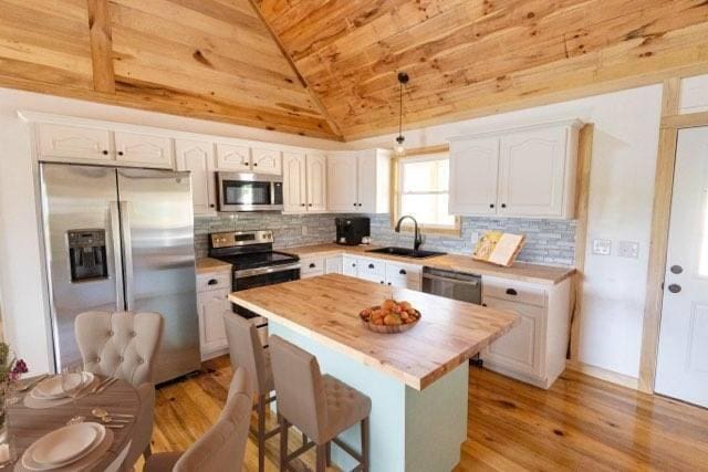 kitchen featuring sink, decorative light fixtures, vaulted ceiling, white cabinets, and appliances with stainless steel finishes