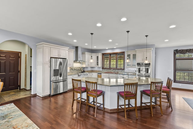 kitchen with stainless steel appliances, a kitchen breakfast bar, dark hardwood / wood-style flooring, wall chimney exhaust hood, and a large island