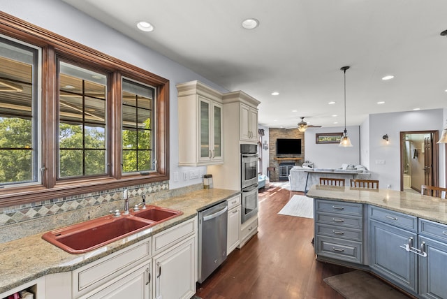 kitchen with hanging light fixtures, a large fireplace, appliances with stainless steel finishes, dark wood-type flooring, and ceiling fan