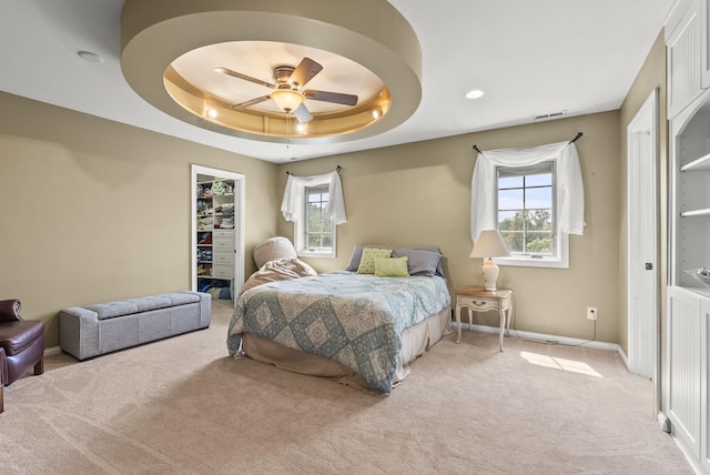 bedroom featuring ceiling fan, a spacious closet, multiple windows, and a tray ceiling