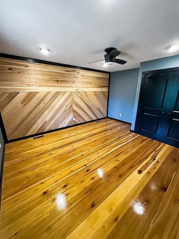 interior space featuring ceiling fan, wood walls, and wood-type flooring