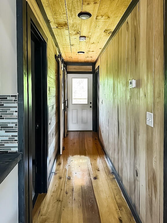 hall featuring wood walls, light wood-type flooring, and wood ceiling