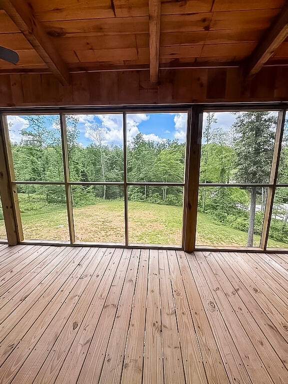 unfurnished sunroom featuring beam ceiling, wood ceiling, and a healthy amount of sunlight