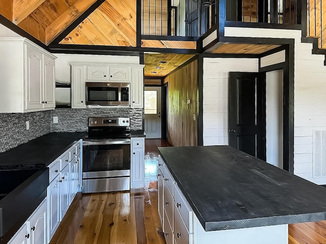 kitchen featuring stainless steel appliances, a center island, dark hardwood / wood-style floors, white cabinetry, and wood walls