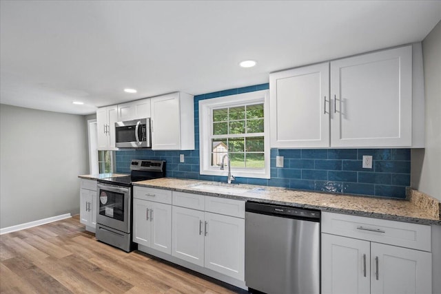 kitchen with light hardwood / wood-style flooring, light stone counters, stainless steel appliances, white cabinetry, and sink