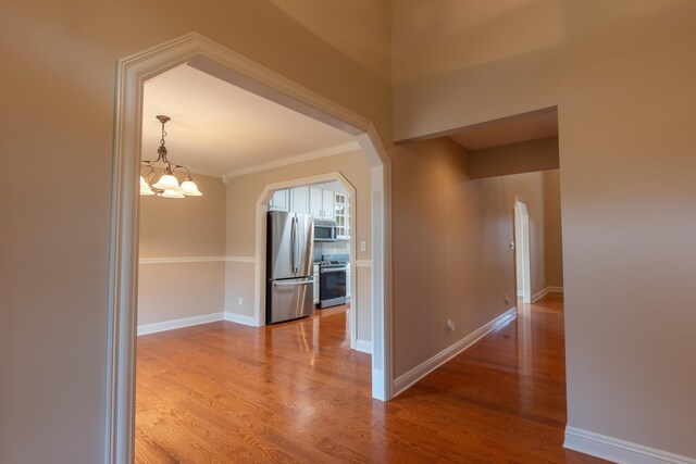 corridor with an inviting chandelier, hardwood / wood-style flooring, and ornamental molding