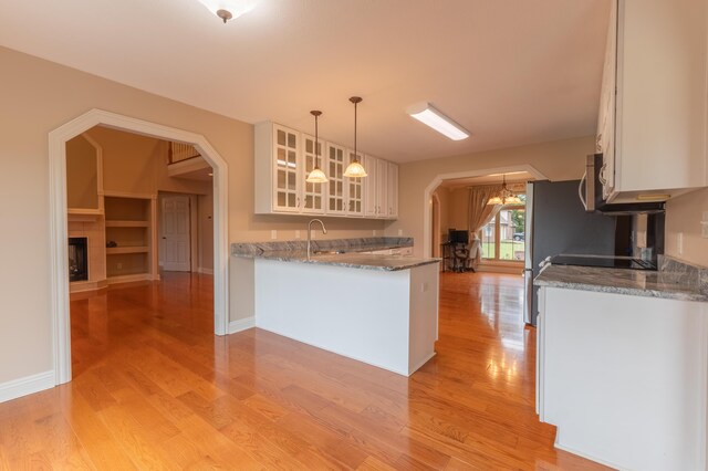 kitchen with white cabinets, hanging light fixtures, sink, dark stone counters, and light wood-type flooring