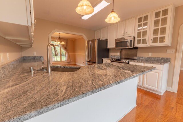 kitchen featuring appliances with stainless steel finishes, hanging light fixtures, white cabinets, kitchen peninsula, and light hardwood / wood-style flooring