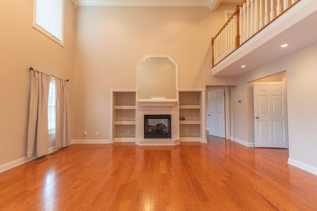 unfurnished living room featuring crown molding, a high ceiling, a tiled fireplace, and hardwood / wood-style floors