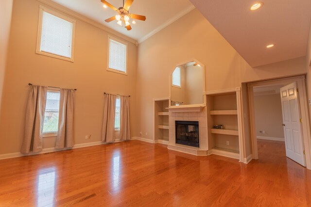 unfurnished living room featuring a tile fireplace, a high ceiling, ceiling fan, ornamental molding, and hardwood / wood-style floors