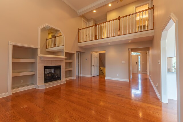 unfurnished living room with built in shelves, crown molding, hardwood / wood-style flooring, a fireplace, and a towering ceiling