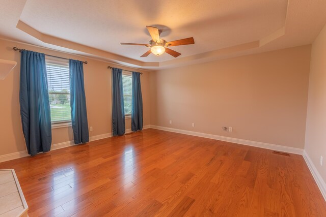 spare room featuring light hardwood / wood-style flooring, ceiling fan, and a raised ceiling