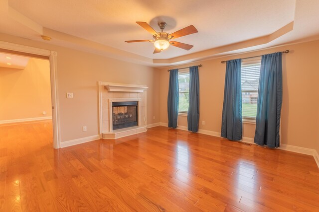 unfurnished living room with a fireplace, a tray ceiling, ceiling fan, and hardwood / wood-style flooring