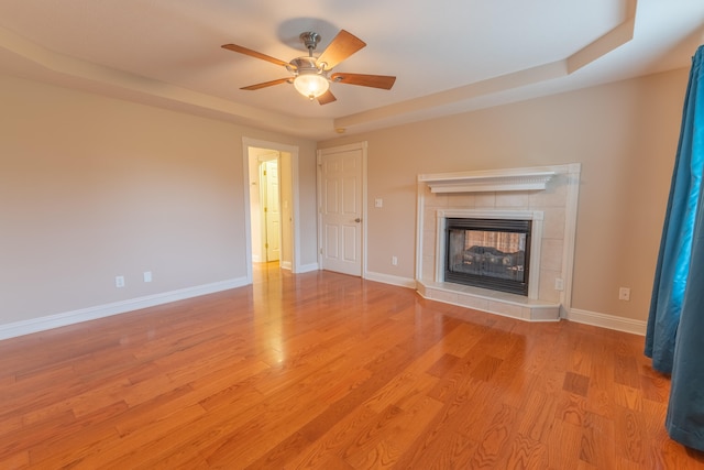 unfurnished living room with ceiling fan, a fireplace, a tray ceiling, and light hardwood / wood-style flooring