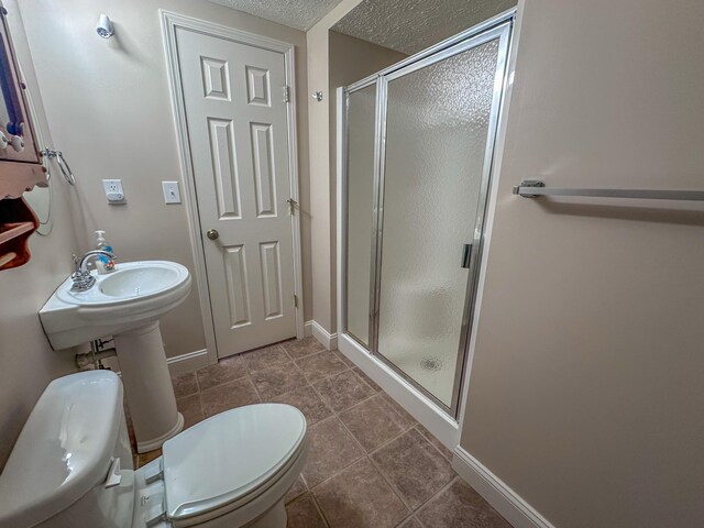 bathroom featuring a textured ceiling, toilet, a shower with door, and tile patterned floors