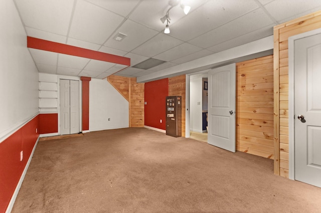 basement with a paneled ceiling, wooden walls, and carpet