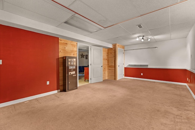 unfurnished room featuring carpet flooring, a paneled ceiling, and wooden walls