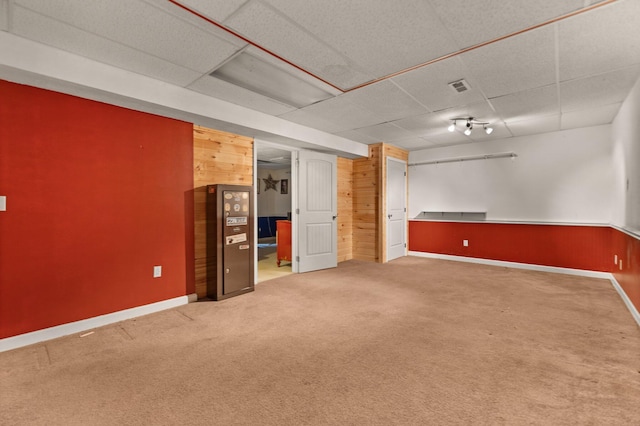 finished basement with a drop ceiling, wood walls, carpet, and baseboards