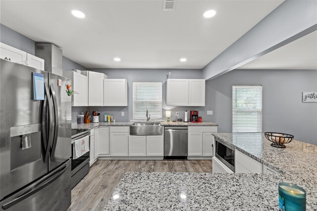 kitchen with white cabinets, light hardwood / wood-style flooring, appliances with stainless steel finishes, light stone counters, and sink