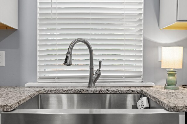 room details with white cabinets, light stone countertops, and sink