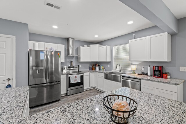 kitchen with stainless steel appliances, wall chimney range hood, sink, light stone countertops, and light hardwood / wood-style floors