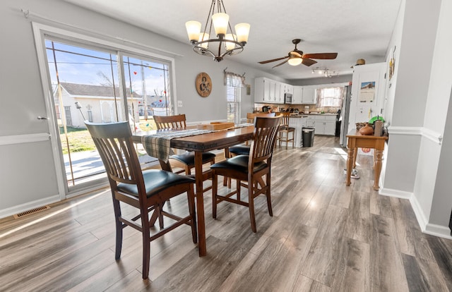 dining space with ceiling fan with notable chandelier, plenty of natural light, and wood-type flooring