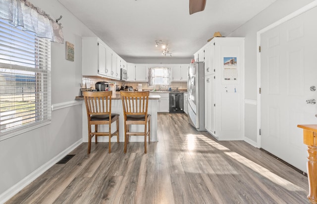 kitchen featuring appliances with stainless steel finishes, tasteful backsplash, kitchen peninsula, hardwood / wood-style flooring, and white cabinets