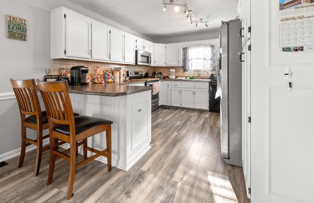 kitchen with tasteful backsplash, wood-type flooring, kitchen peninsula, appliances with stainless steel finishes, and white cabinets