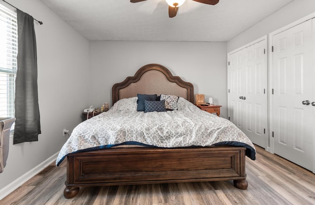 bedroom featuring multiple windows, ceiling fan, wood-type flooring, and two closets