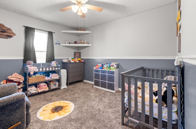 carpeted bedroom with a nursery area, ceiling fan, and a textured ceiling