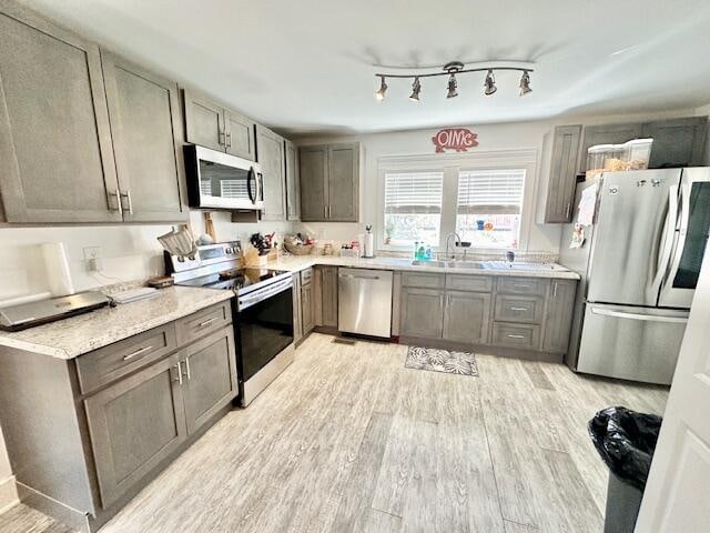 kitchen with gray cabinets, appliances with stainless steel finishes, sink, and light hardwood / wood-style flooring