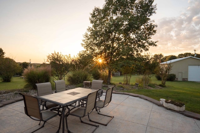 patio terrace at dusk featuring a garage, a lawn, and an outbuilding