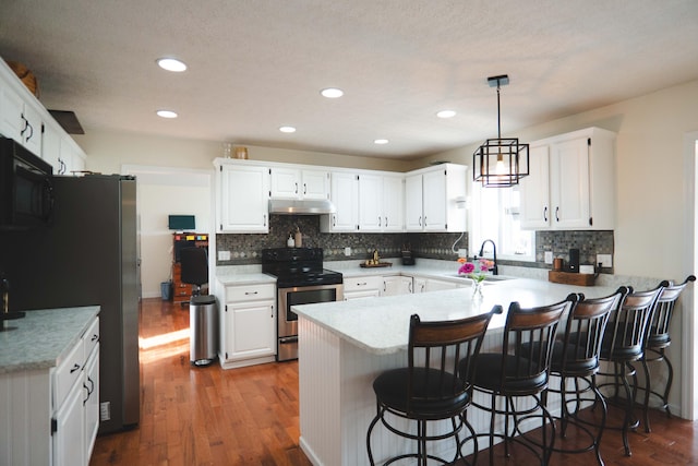 kitchen featuring hardwood / wood-style floors, appliances with stainless steel finishes, white cabinetry, kitchen peninsula, and a breakfast bar area