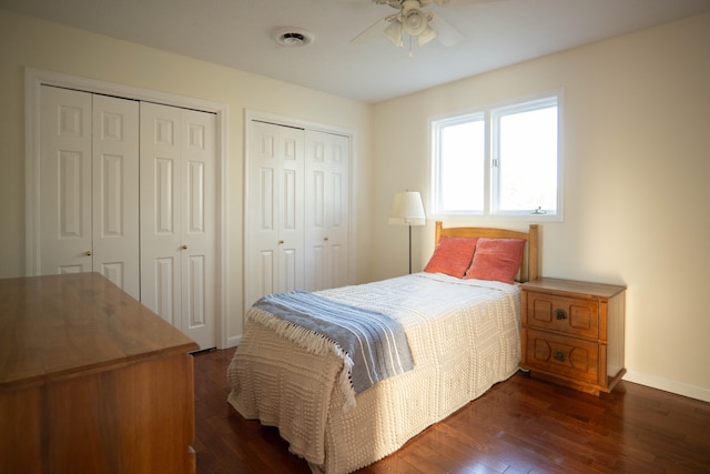 bedroom with dark wood-type flooring, two closets, and ceiling fan