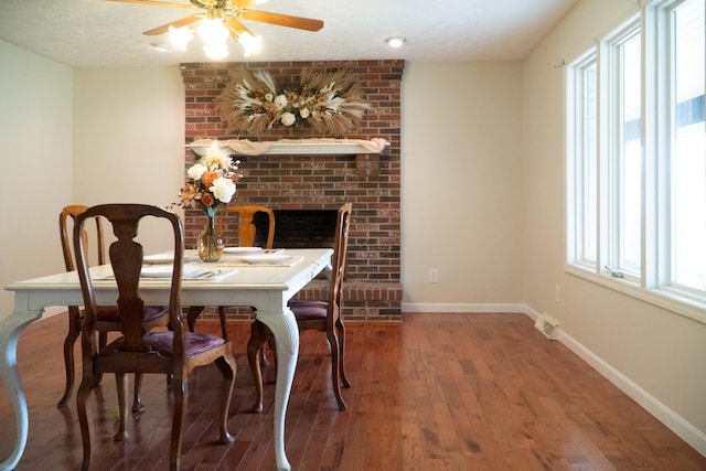 dining space with hardwood / wood-style floors, ceiling fan, a textured ceiling, and a brick fireplace