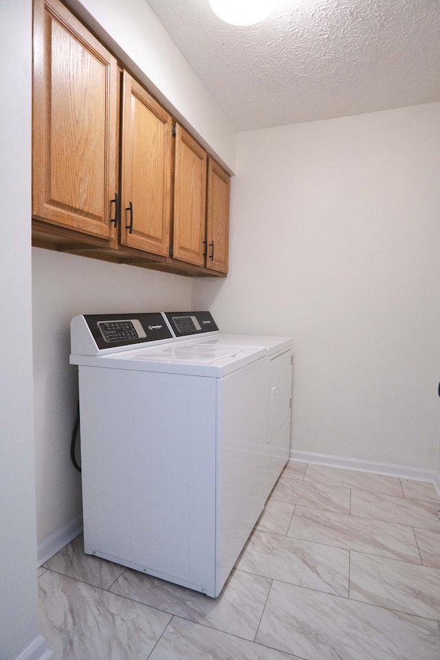 clothes washing area with washing machine and clothes dryer, cabinets, and a textured ceiling