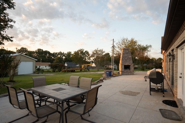 patio terrace at dusk featuring an outbuilding, grilling area, an outdoor stone fireplace, a lawn, and a garage