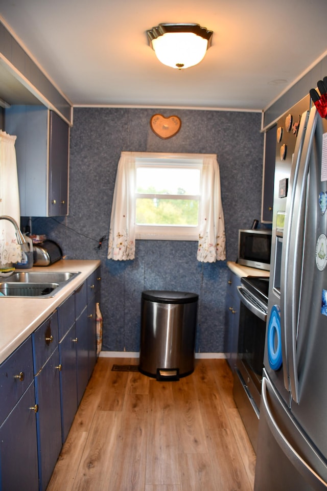 kitchen with blue cabinetry, stainless steel appliances, sink, and light hardwood / wood-style floors