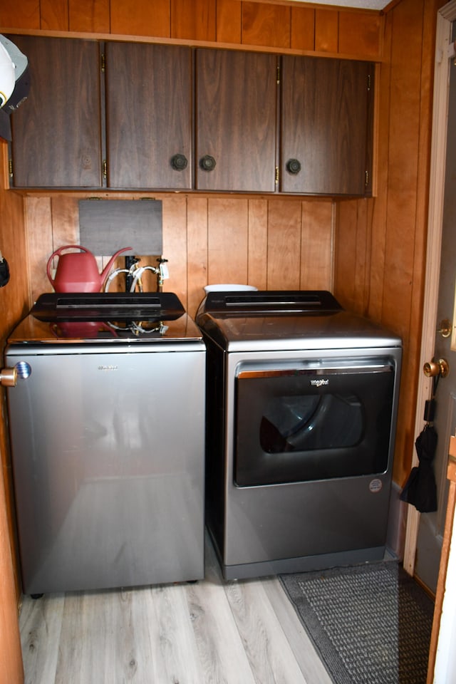 laundry area featuring wooden walls, separate washer and dryer, cabinets, and light hardwood / wood-style flooring