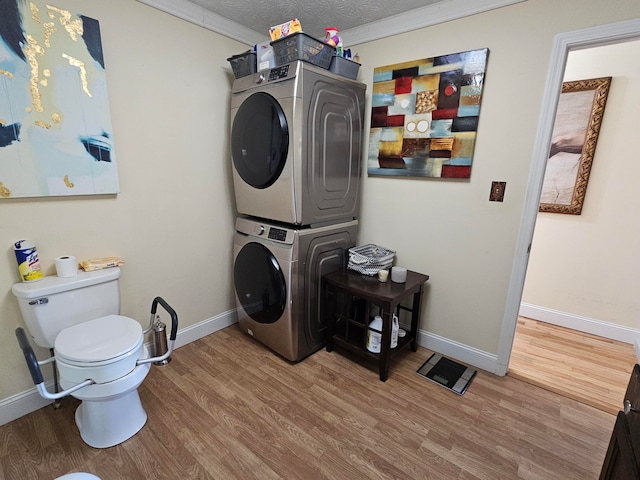 washroom with ornamental molding, a textured ceiling, hardwood / wood-style floors, and stacked washer and dryer